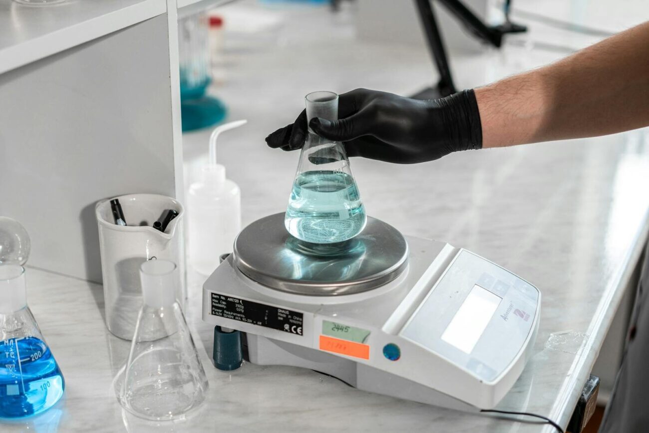 Researcher placing a flask on a laboratory balance scale for precise weight measurement illustrating the type of precision weighing used for plant and biomass sample analysis in ecological research.