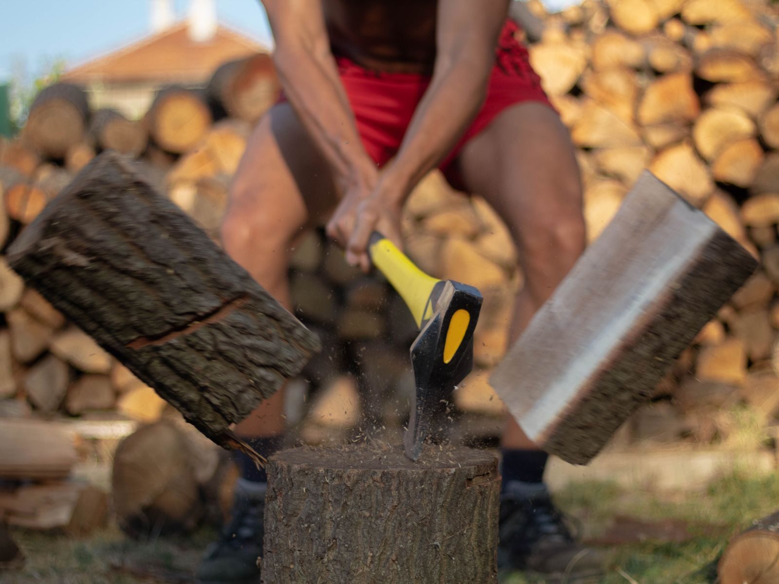 Person splitting a log with an axe on a chopping block beside a woodpile