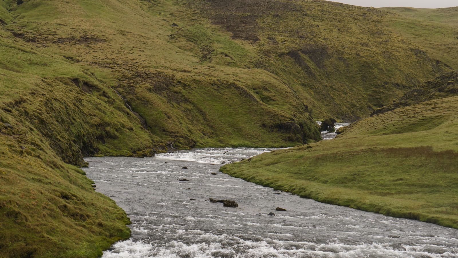 A river running through open hill country, carrying water and dissolved material away across the landscape