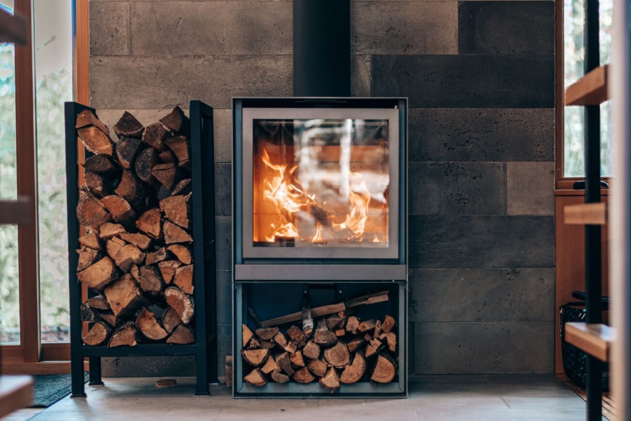 Modern wood burning stove alight with neatly stacked logs stored beside and below it