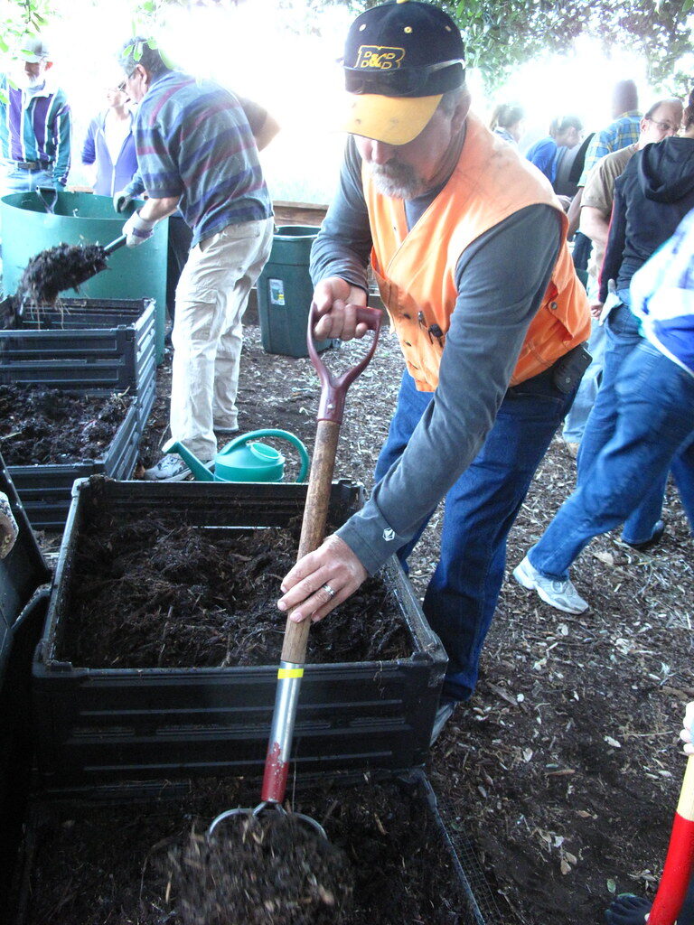 Person turning dark compost in a bin with a garden fork