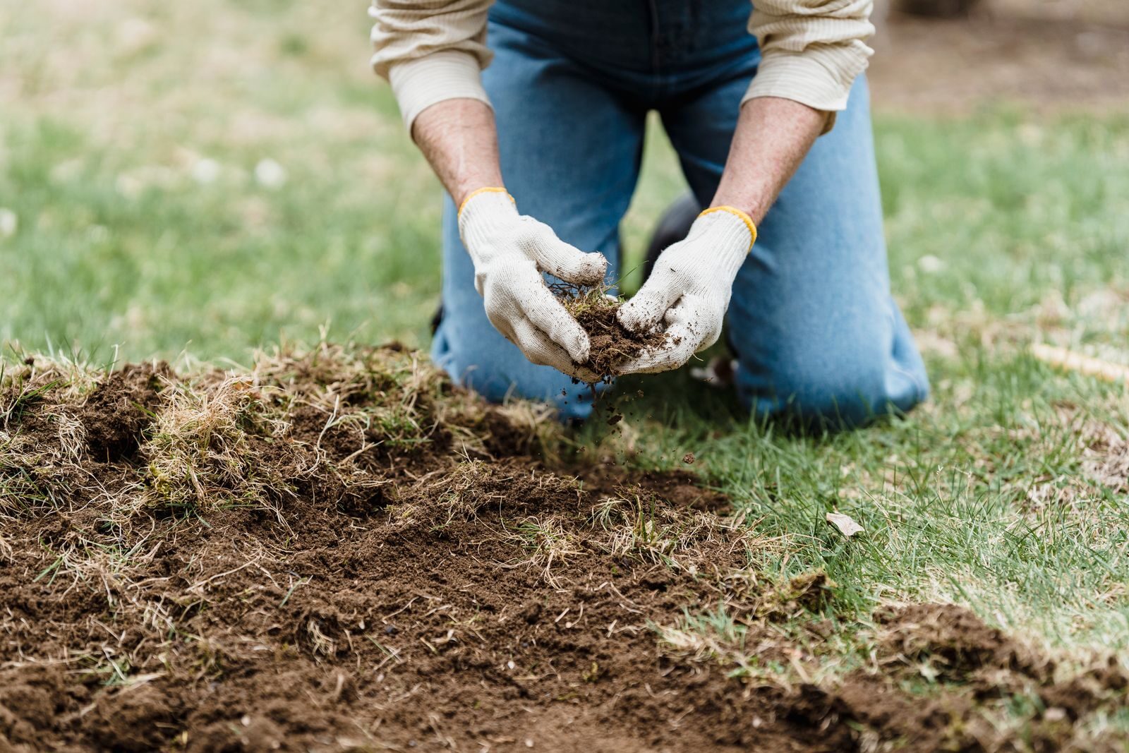 Person crouching and examining garden soil by hand to check its condition