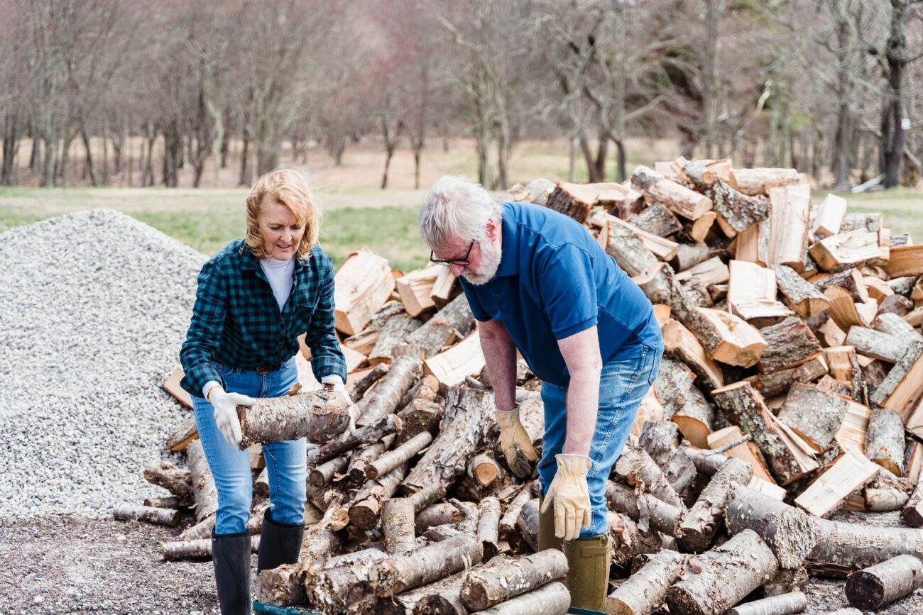 Two people handling and stacking split firewood beside a large woodpile
