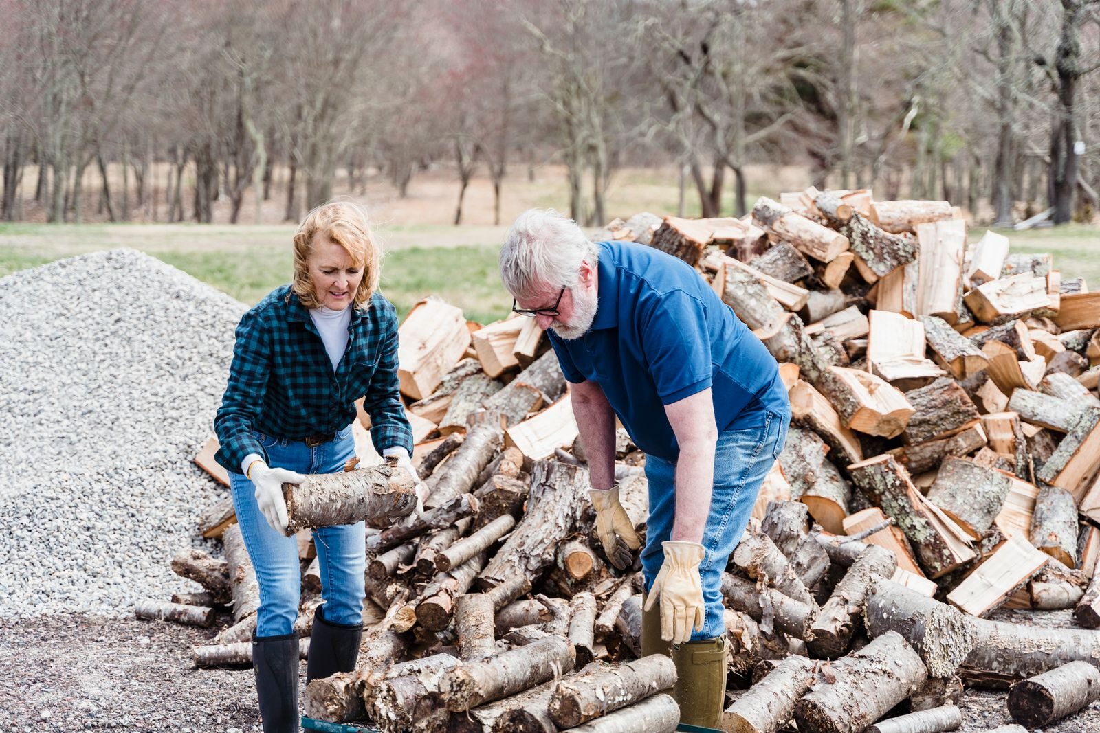 Two people handling and stacking split firewood beside a large woodpile