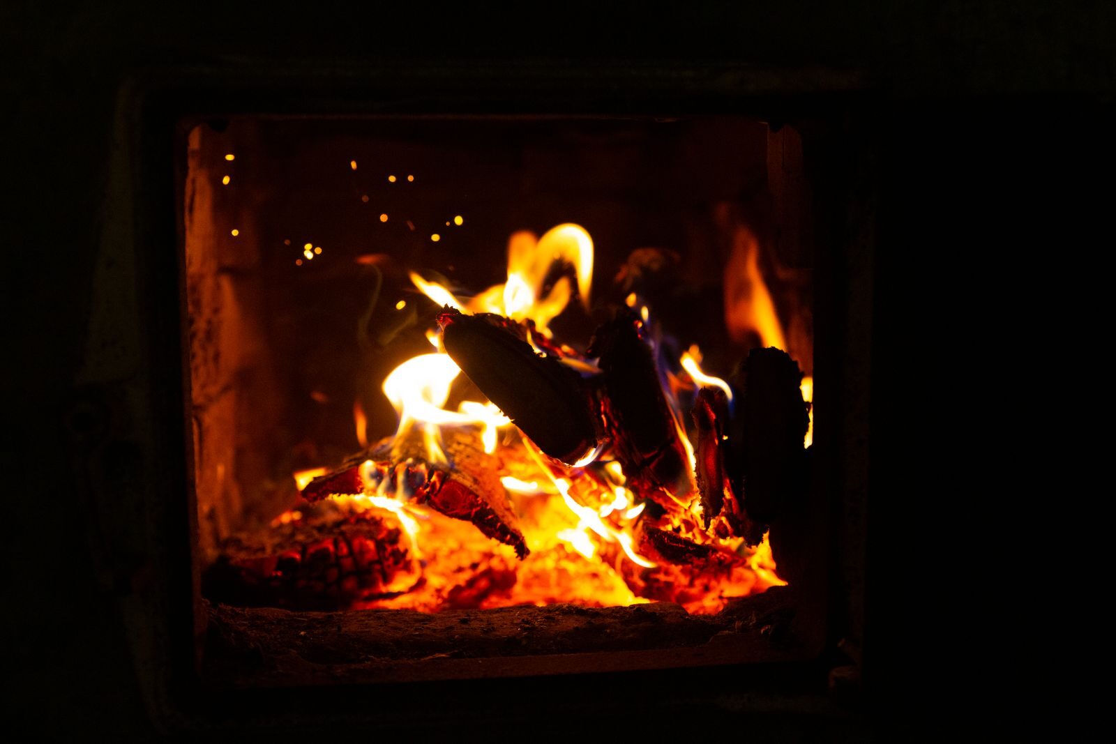 Logs burning with flames and a glowing bed of coals inside a wood stove